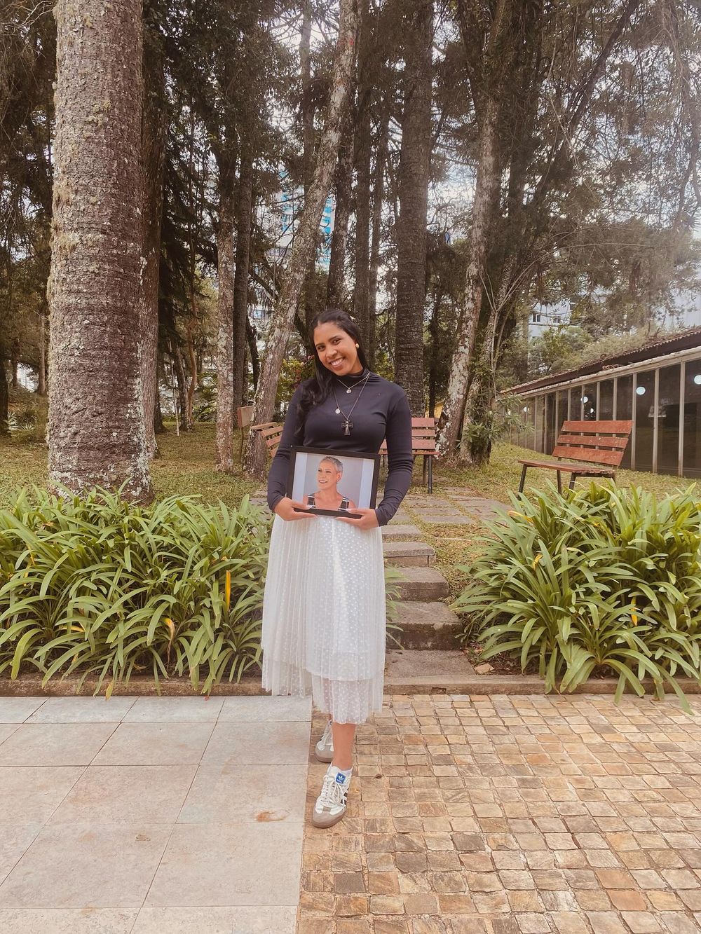 Chayanny em um jardim de araucárias segurando o retrato emoldurado de sua mãe, Fátima